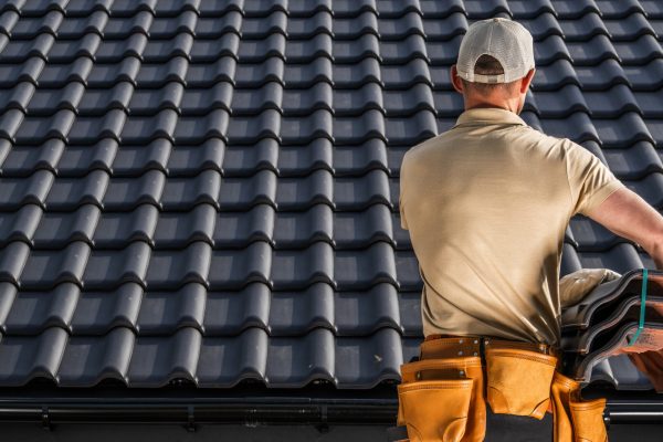 Professional Caucasian Roofing Contractor Worker Moving a Black Roof Ceramic Tiles in His Hands